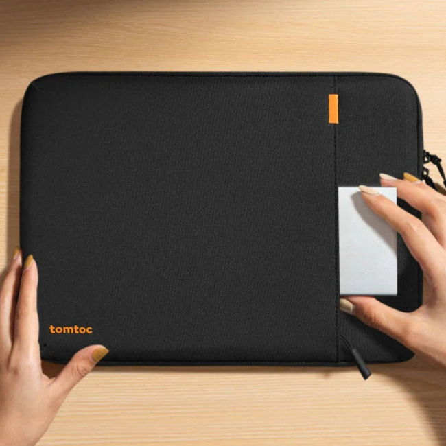 Person holding a black laptop sleeve on a desk with office supplies.